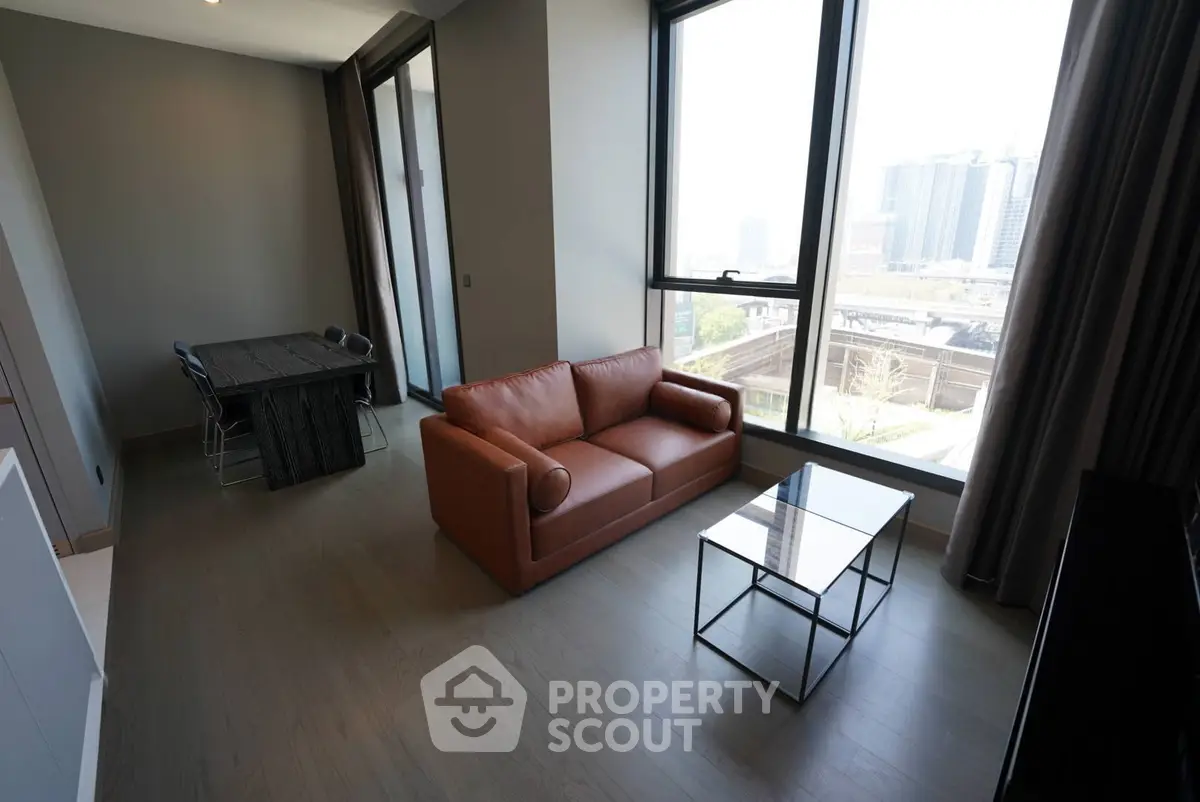Modern living room with large windows and city view, featuring a stylish sofa and dining area.