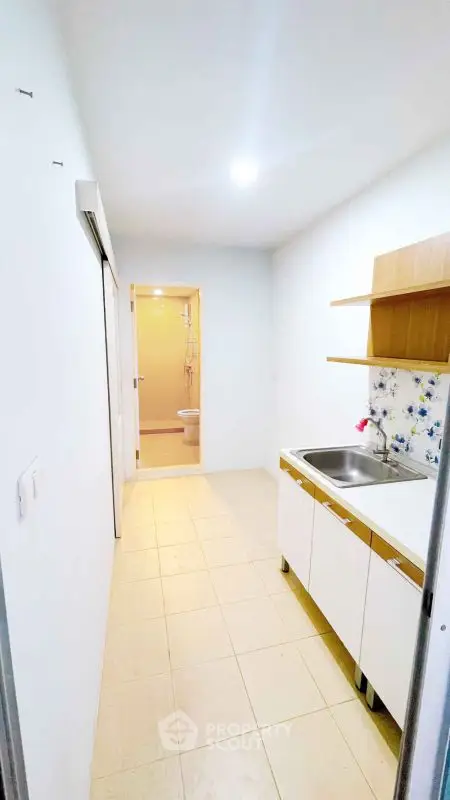 Compact kitchen with white cabinets and floral backsplash leading to a bathroom