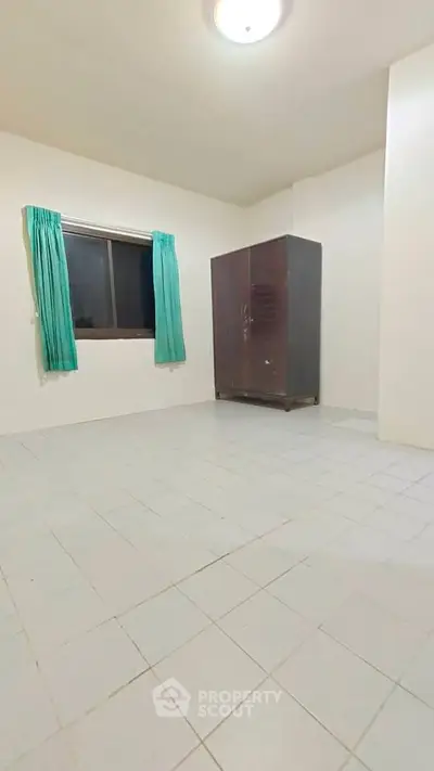 Spacious empty room with tiled floor and large window, perfect for customization.