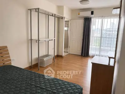 Spacious bedroom with wooden flooring and large window offering natural light.