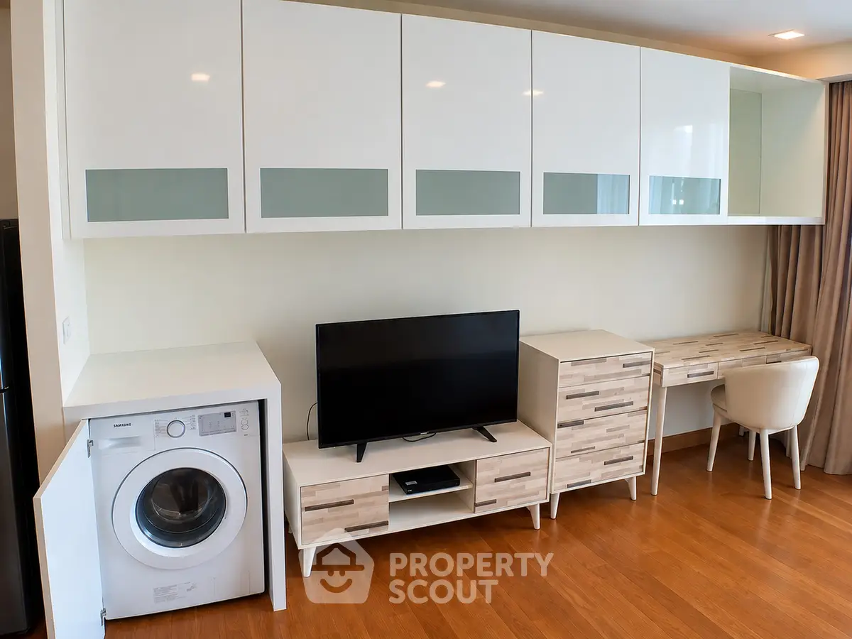 Modern living room with sleek cabinetry, TV, and washing machine in a stylish apartment.