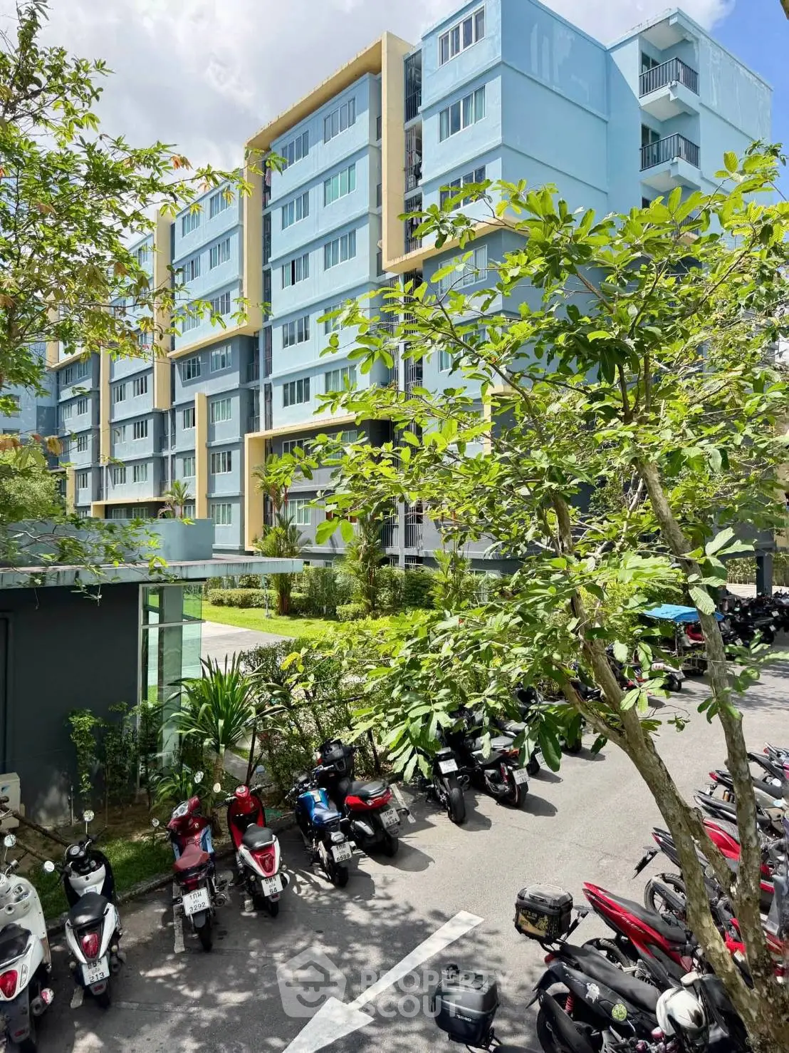 Modern residential building with lush greenery and motorbike parking area.