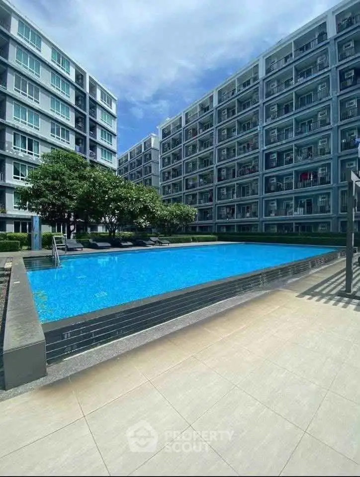 Modern apartment complex with a sparkling pool and lush greenery under a clear blue sky.