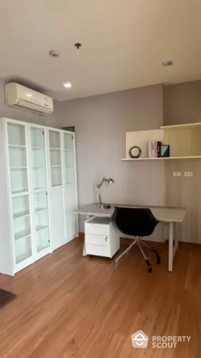 Modern study room with sleek desk, chair, and glass cabinet in a bright apartment.