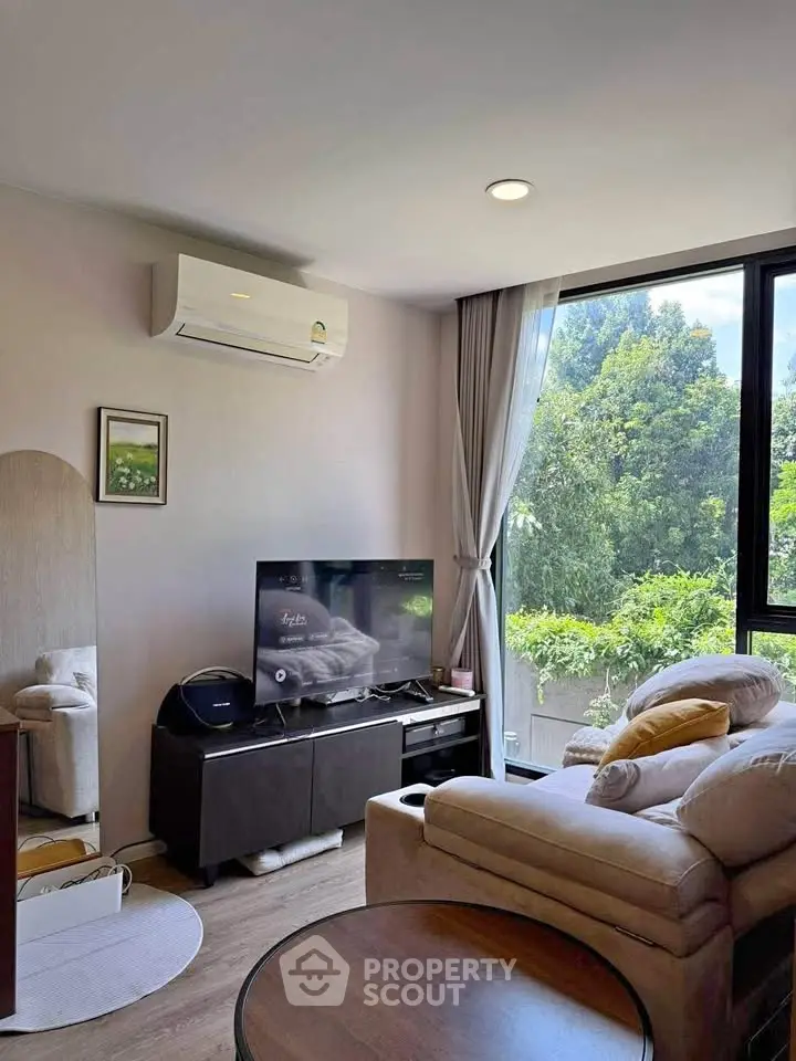Cozy living room with large window and lush greenery view, featuring modern furniture and air conditioning.