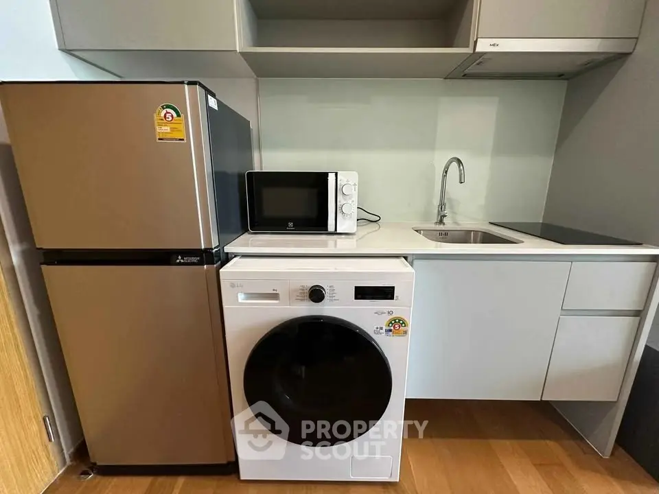 Modern kitchen with sleek appliances including fridge, washing machine, and microwave in compact layout.