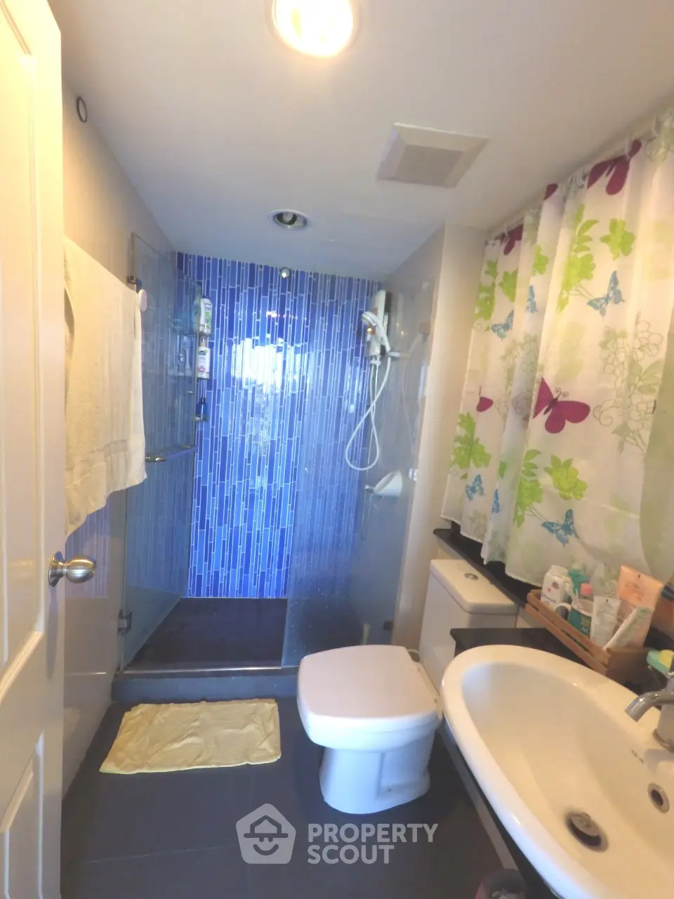 Modern bathroom with glass shower and vibrant blue tiles, featuring sleek fixtures and colorful shower curtain.