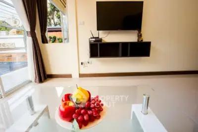 Modern living room with wall-mounted TV and pool view, featuring a glass coffee table with fruit.