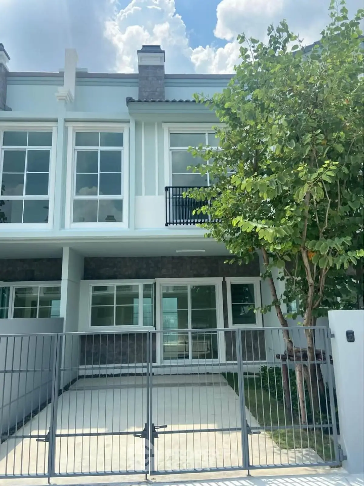 Modern townhouse with large windows and gated driveway, surrounded by lush greenery.