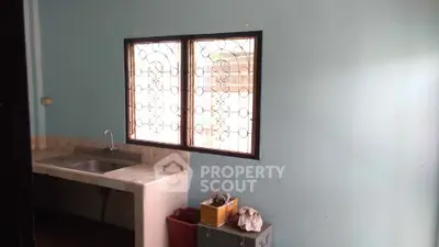 Simple kitchen with metal sink and barred window in a modest home.
