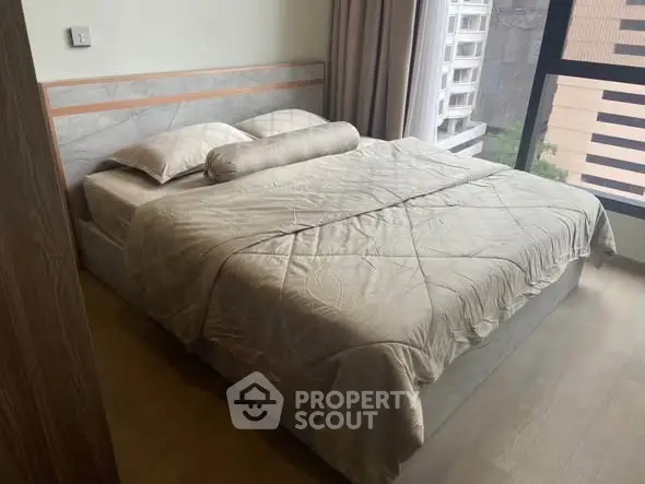 Spacious bedroom with large window offering city view, featuring a comfortable bed and modern decor.