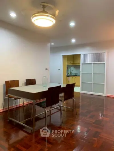 Spacious dining area with modern lighting and wooden flooring adjacent to a kitchen.