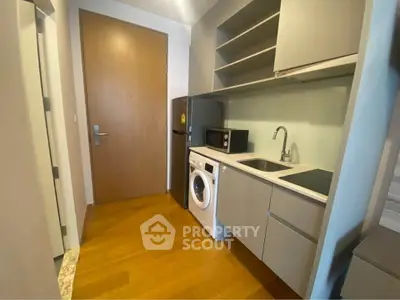 Compact modern kitchen with washing machine and microwave, sleek cabinetry and wooden flooring.