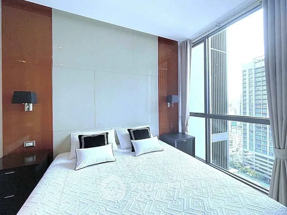 Luxurious bedroom with large windows offering stunning city views, modern decor, and elegant lighting.