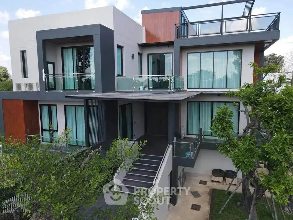 Modern luxury villa with large windows and spacious balconies surrounded by lush greenery.