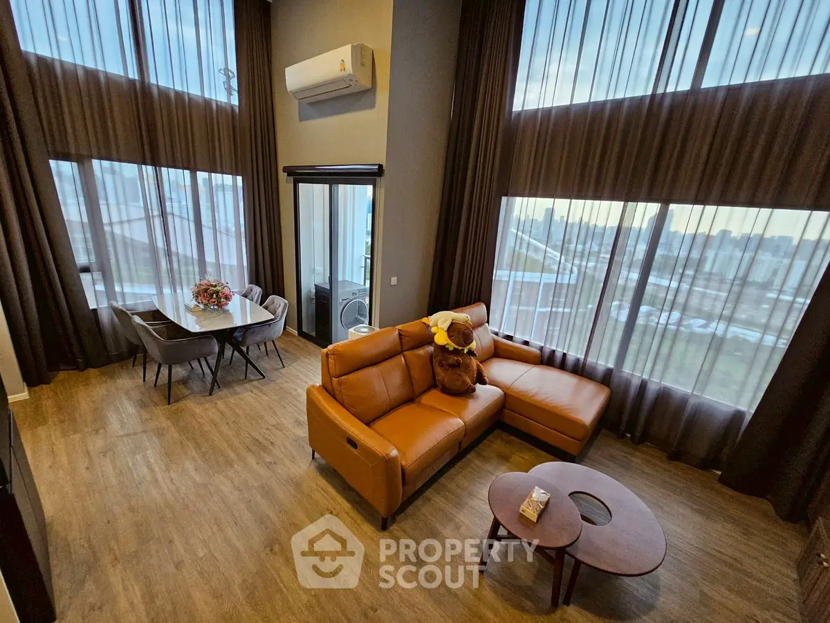 Luxurious high-ceiling living room with leather sofa and dining area, featuring large windows and modern decor.