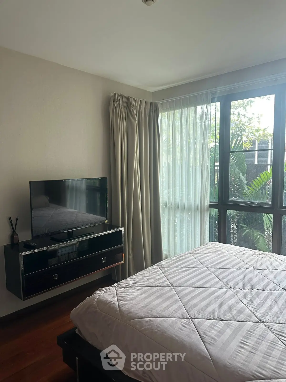 Cozy bedroom with large window and modern TV setup, perfect for relaxation.
