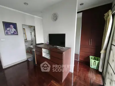 Cozy bedroom with wooden flooring, TV stand, and bathroom access in a modern apartment.