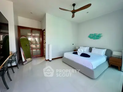 Spacious bedroom with modern decor and natural light, featuring a large bed and stylish ceiling fan.