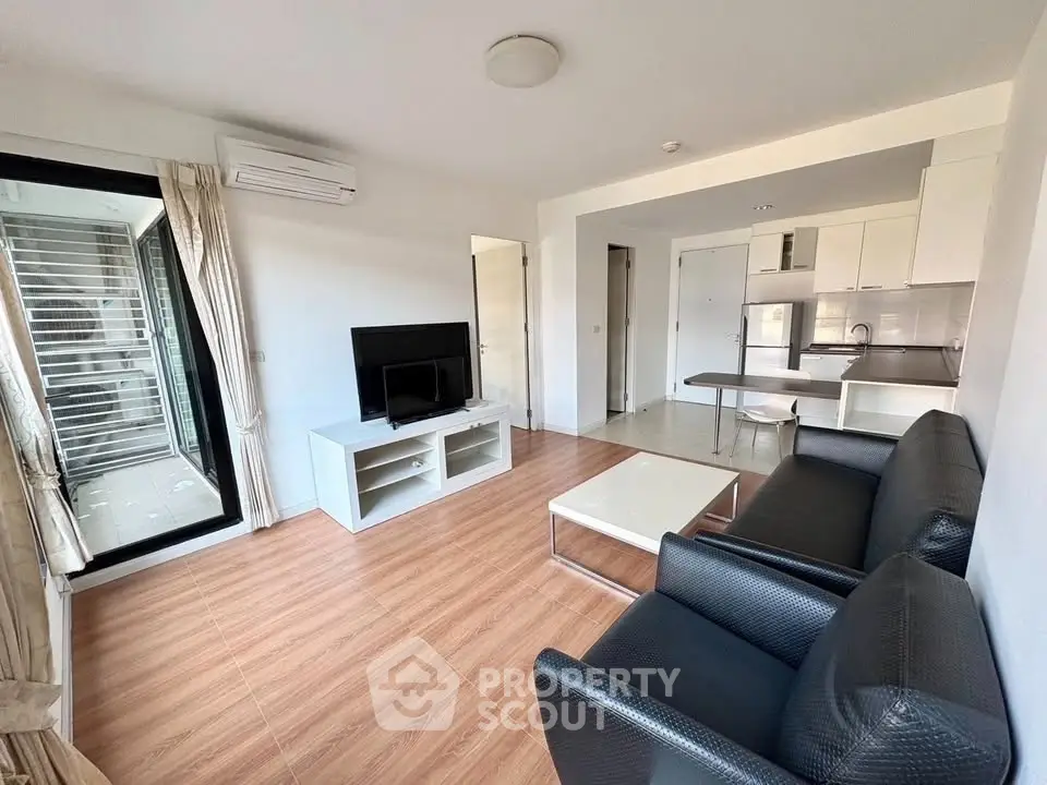 Modern living room with open kitchen, sleek furniture, and wooden flooring in a bright apartment.