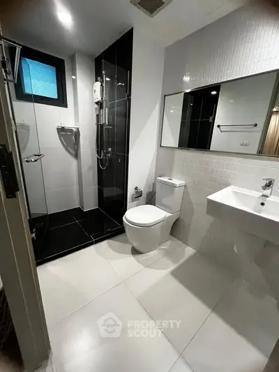Modern bathroom with sleek black and white design, featuring a glass shower and contemporary fixtures.