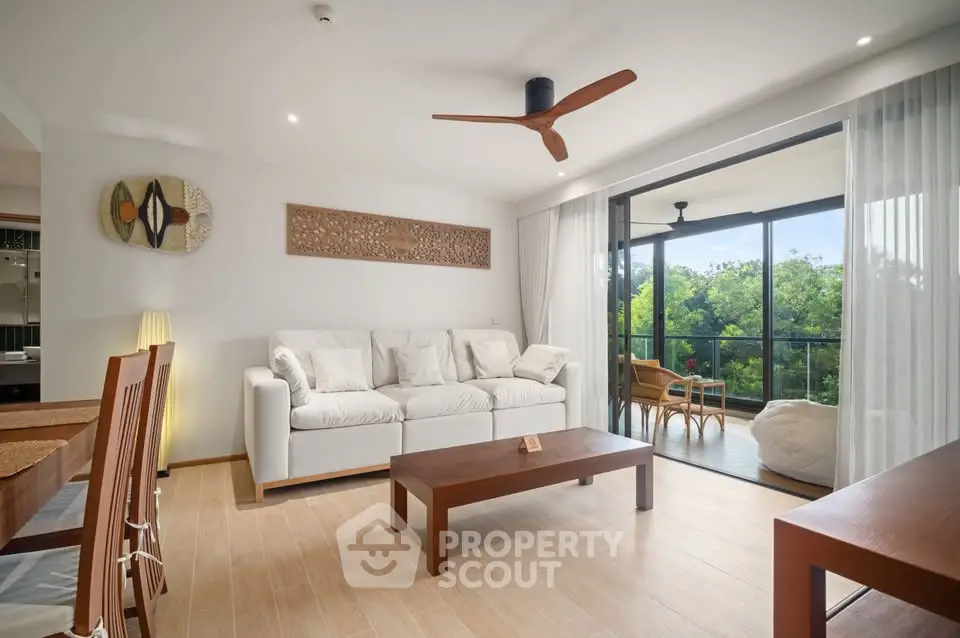 Spacious living room with modern decor and large balcony overlooking lush greenery.