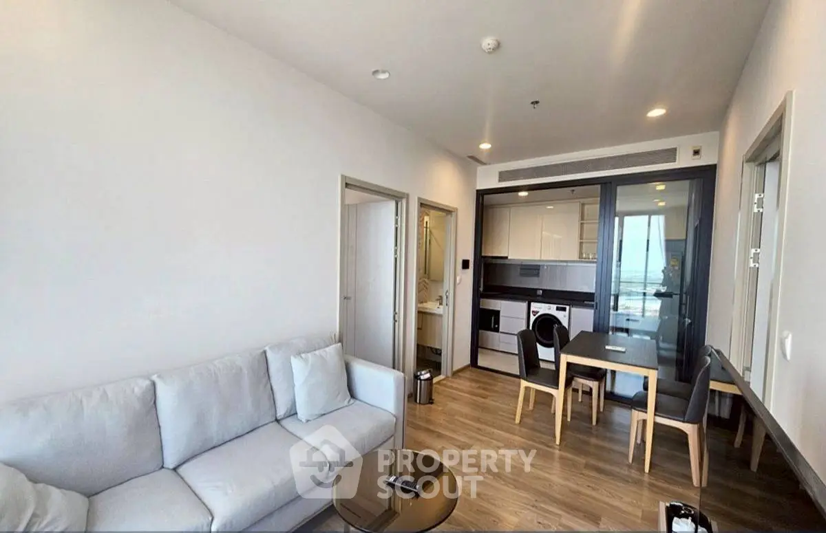 Modern living room with open kitchen, featuring sleek furniture and a cozy ambiance.