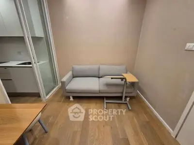 Cozy living room with modern sofa and wooden flooring, adjacent to a compact kitchen.