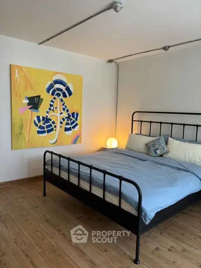Modern bedroom with stylish artwork and cozy lighting, featuring a metal bed frame and wooden flooring.