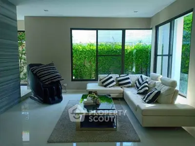 Modern living room with sleek furniture and large windows overlooking lush greenery.