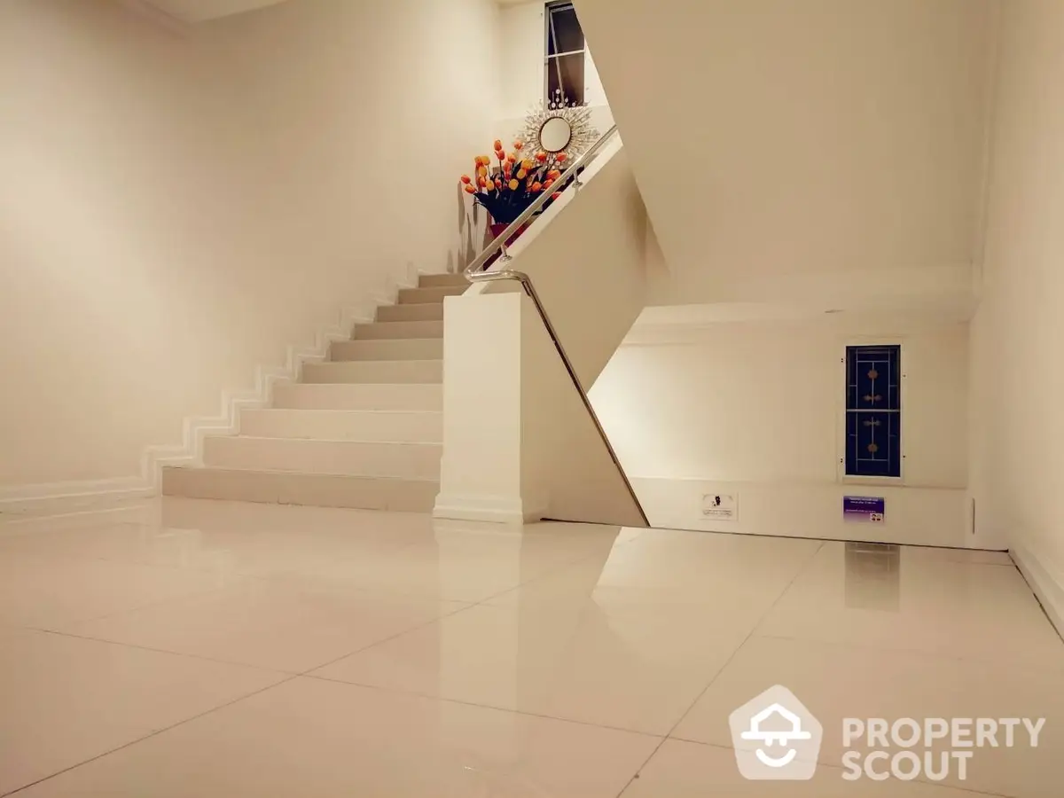 Elegant minimalist interior with a sweeping staircase and pristine white tiled floors, perfect for modern living.