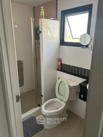 Modern bathroom with shower and toilet, featuring sleek black and white tiles and a small window for natural light.