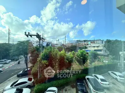 Scenic urban view from a window showcasing lush greenery and parked cars under a bright blue sky.