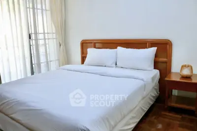 Cozy bedroom with wooden headboard and natural light through sheer curtains.