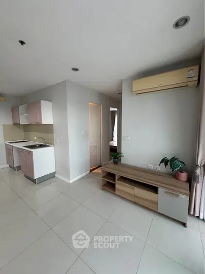 Modern apartment interior with open kitchen and living area, featuring sleek cabinetry and air conditioning.