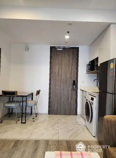 Modern apartment interior with compact kitchen and dining area, featuring washing machine and fridge.