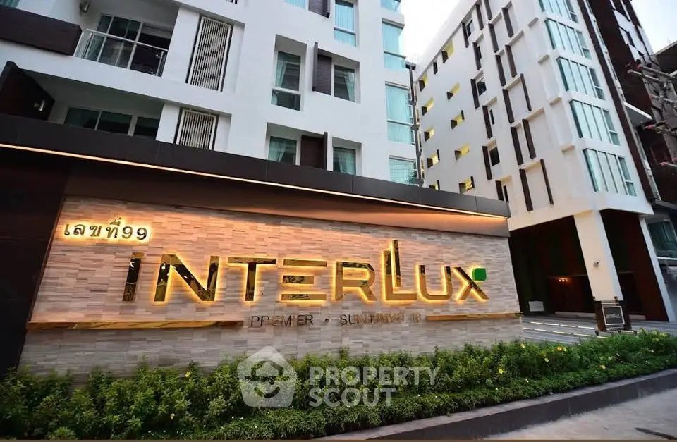 Modern apartment building exterior with stylish signage and lush greenery at entrance.