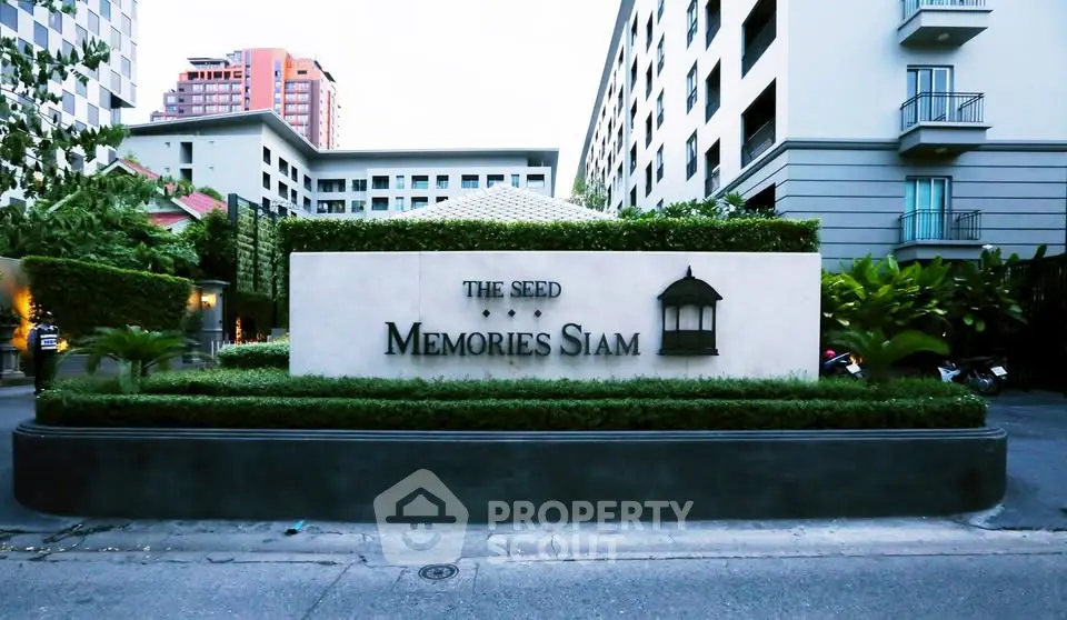 Modern condominium entrance with lush greenery and elegant signage in urban setting.