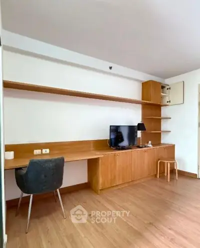 Modern study room with wooden desk, shelves, and TV in a stylish apartment.