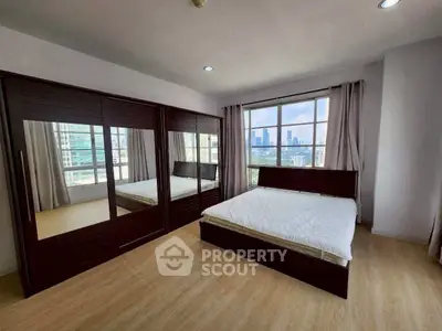 Spacious bedroom with city view, featuring large mirrored wardrobe and wooden flooring.