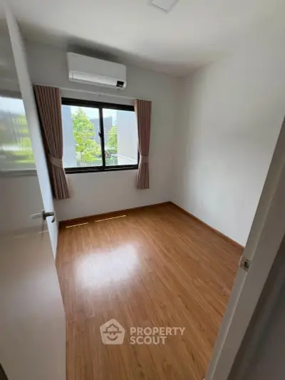 Spacious empty room with wooden flooring and large window, perfect for customization.