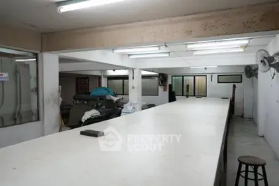 Spacious industrial-style interior with long workbench and fluorescent lighting, ideal for creative workspace or storage.