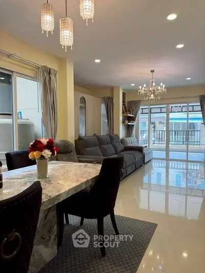 Spacious living room with elegant chandelier and marble dining table, featuring large windows for natural light.