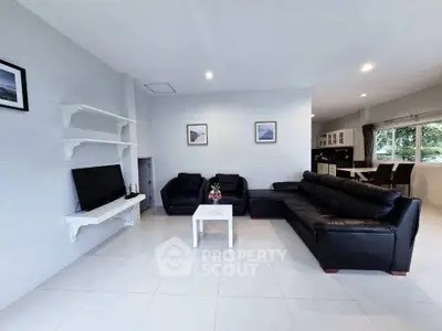 Spacious modern living room with sleek black leather sofas and wall-mounted TV.