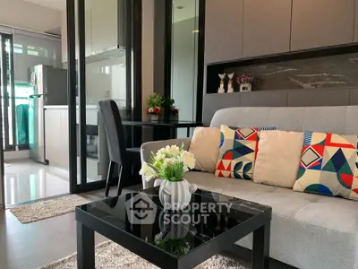 Modern living room with stylish sofa and vibrant cushions, adjacent to sleek kitchen with glass partition.