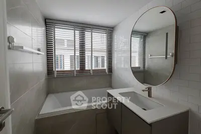 Modern bathroom with sleek design, featuring a large round mirror and bathtub under natural light.