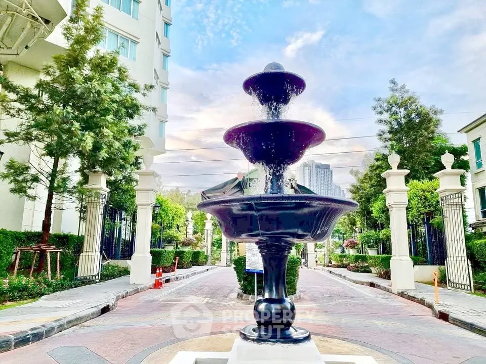 Elegant entrance with a grand fountain in a luxurious residential complex, surrounded by lush greenery and modern architecture.