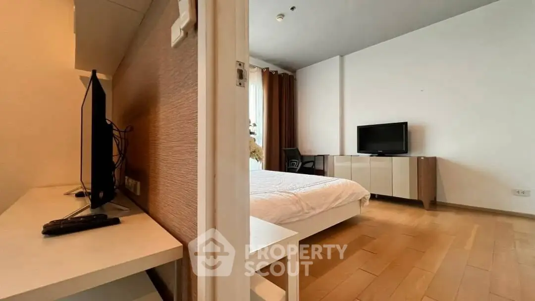 Modern bedroom with wooden flooring and TV, featuring a sleek design and natural light.