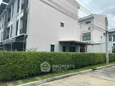 Modern townhouse exterior with lush green hedge and paved pathway in a serene neighborhood.