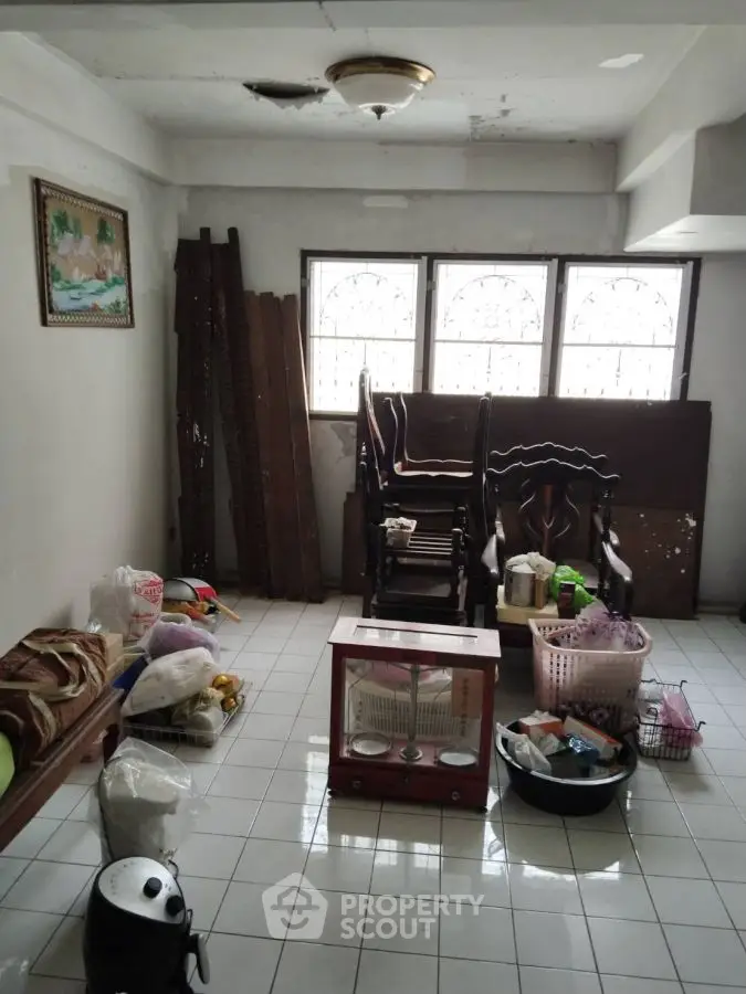Cluttered room with chairs, bags, and household items on tiled floor.
